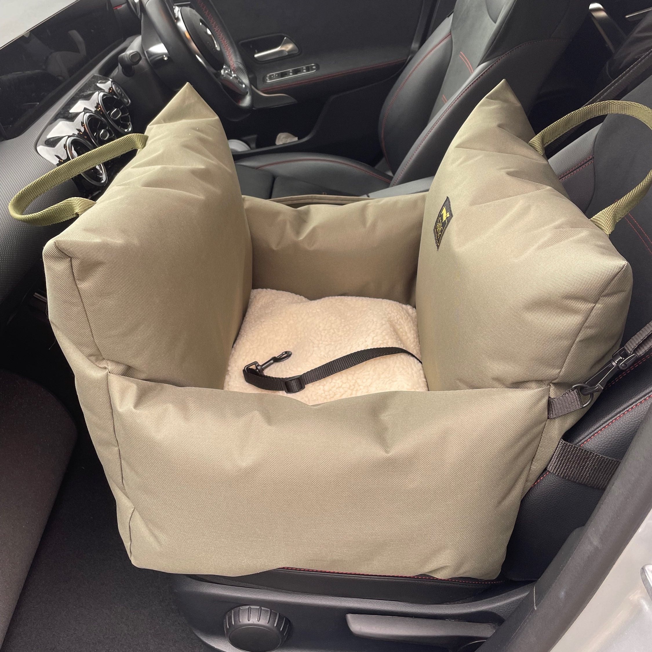 A luxury dog car seat in stone color, placed in the front seat of a car, with a waterproof exterior and a sherpa fleece cushion inside.