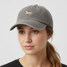 A washed brown baseball cap featuring an embroidered dachshund logo on the front, displayed on a textured tan surface.