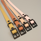 Four leather dog collars in different colors with black buckles on a brown surface.