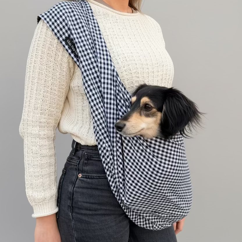 Person holding a dog in a checkered sling against a brick wall.